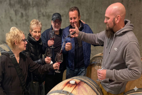 A winemaker using a wine thief to pour red wine for a group of guests during an exclusive barrel room tasting in the Willamette Valley.