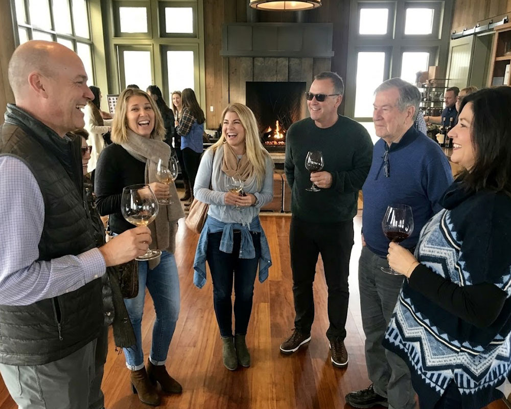 A group of friends laughing and enjoying glasses of wine together inside a cozy tasting room with a fireplace during a Willamette Valley wine tour.